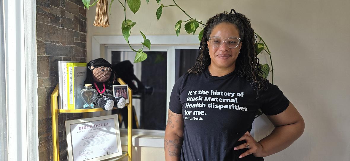 A young Black woman in glasses stands hand on hip inside a doula clinic