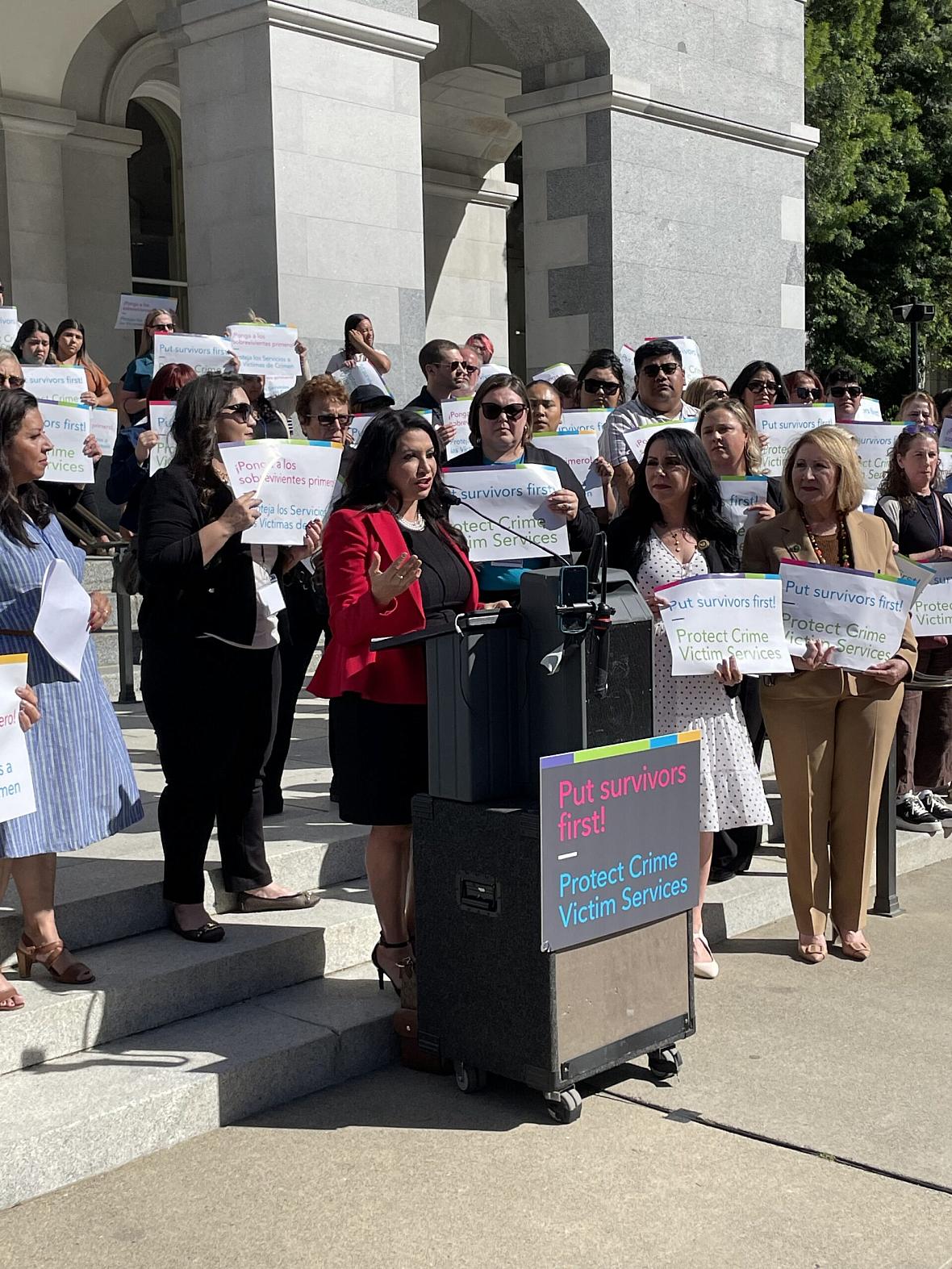 People with posters gathered around someone speaking on a podium