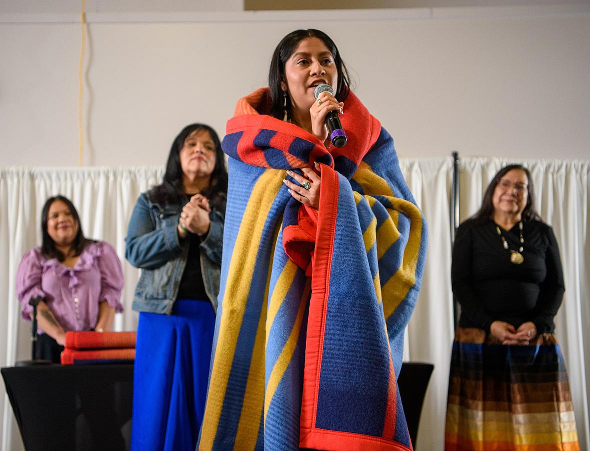 Huwighurruk Tribal Health Program graduate Desirae Barragan, wrapped in a colorful blanket, introduces herself in her native language during the Huwighurruk blanket ceremony in 2025. 