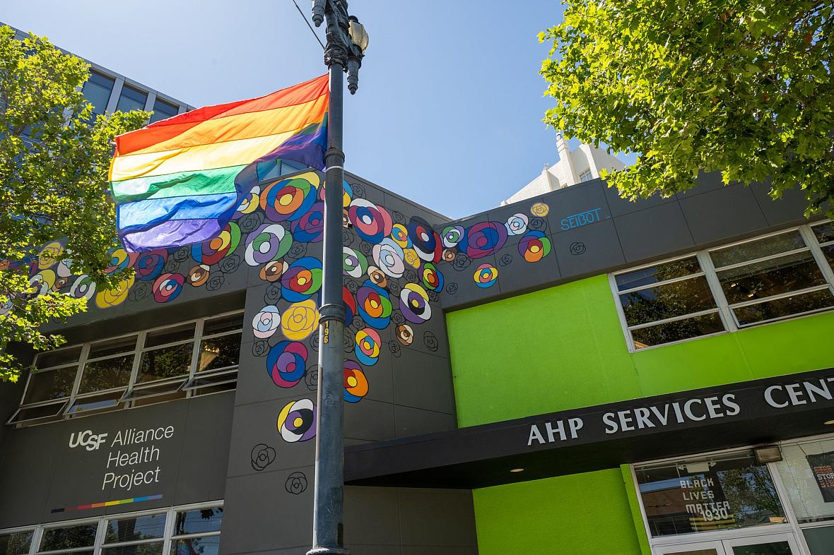 A rainbow flag flies in front of two buildings in San Francisco, including UCSF Alliance Health Project