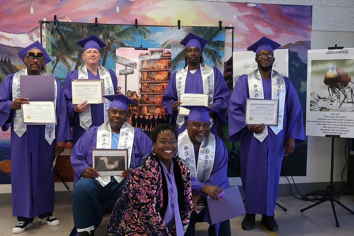 Six graduates in purple gowns hold up their diplomas