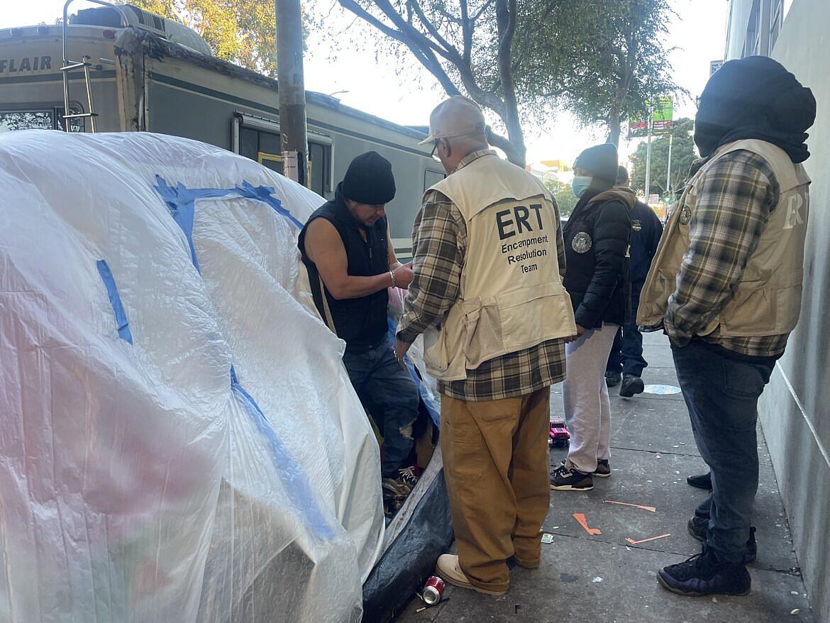 People in ERT (Encampment Resolution team) uniform around a guy near homeless shelter