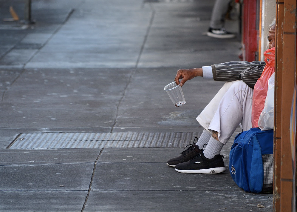 Person sitting on a sidewalk holding a cup 