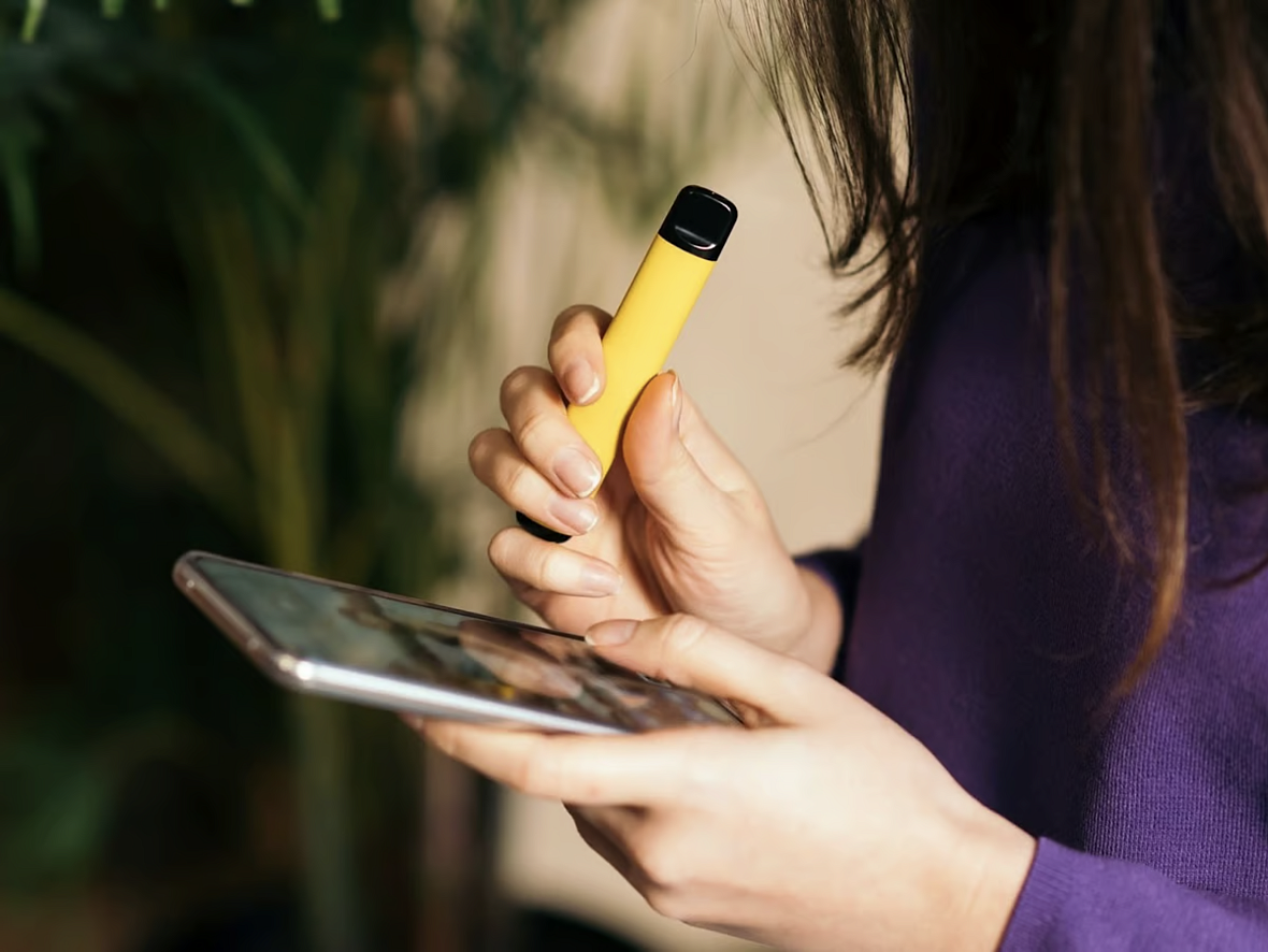 Person with yellow vape in one hand and phone in the other