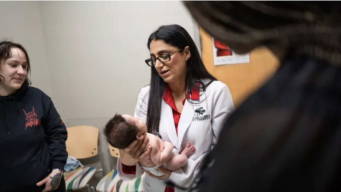 Person in a doctor's coat holding a baby