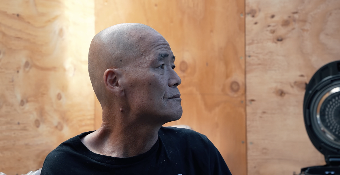An older balding Korean man sits in profile inside a community shelter in Los Angeles