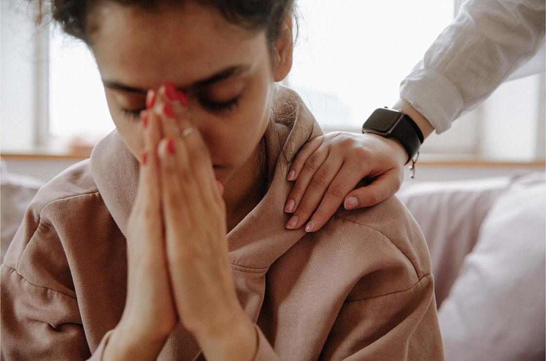 A young South Asian Indian Woman buries her face in her hands as a therapist comforts her.