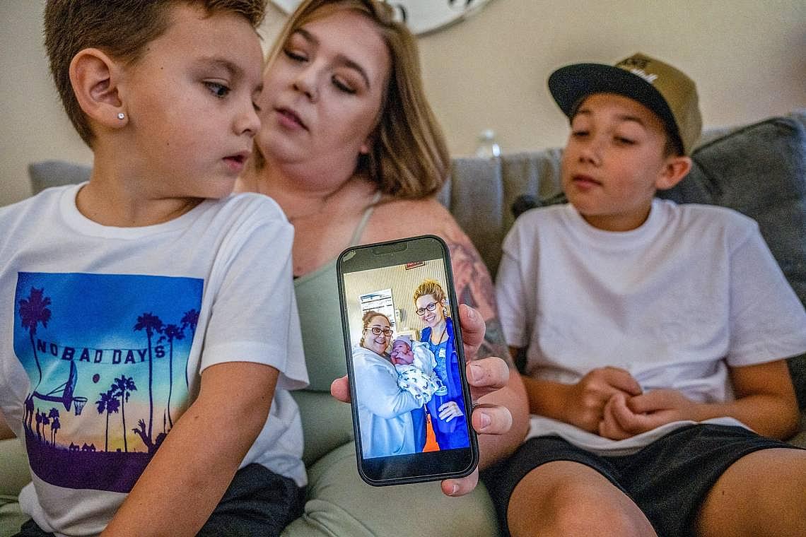 A mom showing photo of her newborn while seating with her children