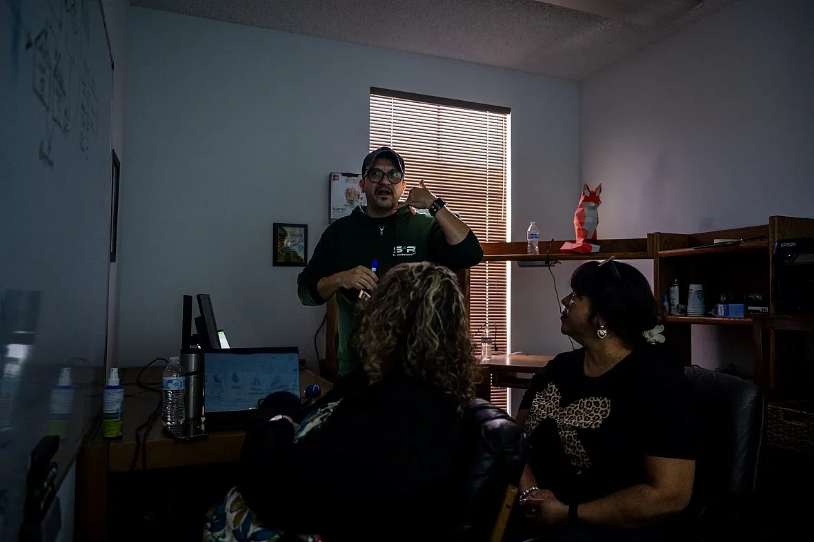 A man leads a discussion in a dimly lit office as two women listen.