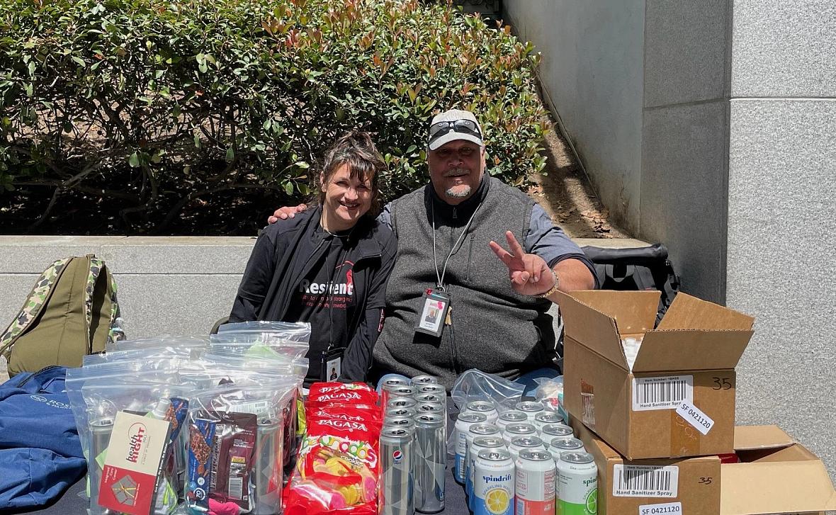 Two people posing with soda cans, chips, and other items