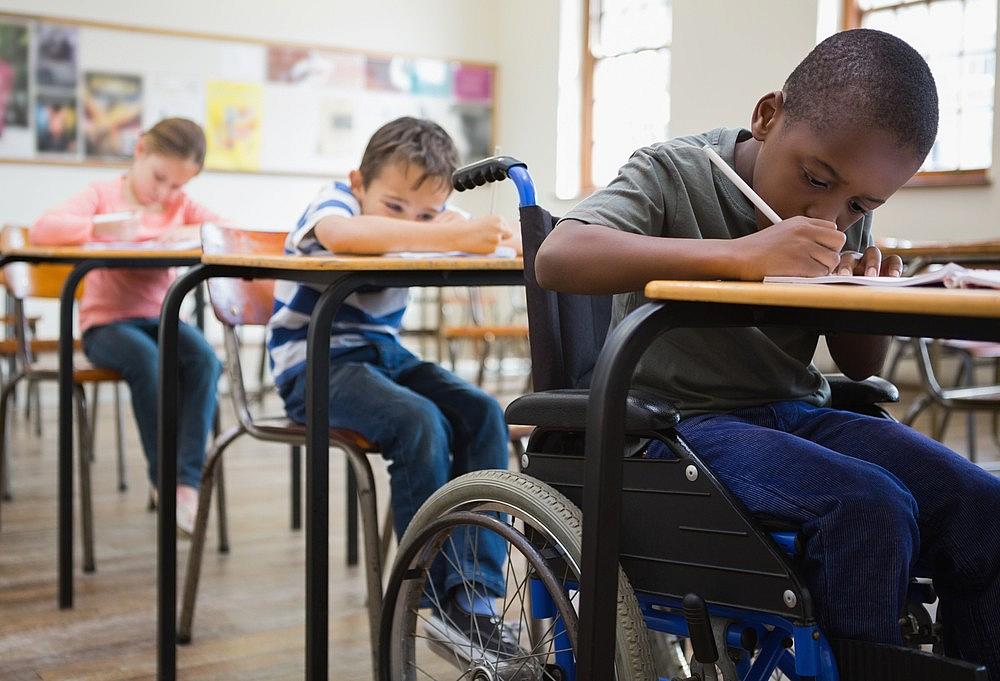 3 children in a classroom, writing