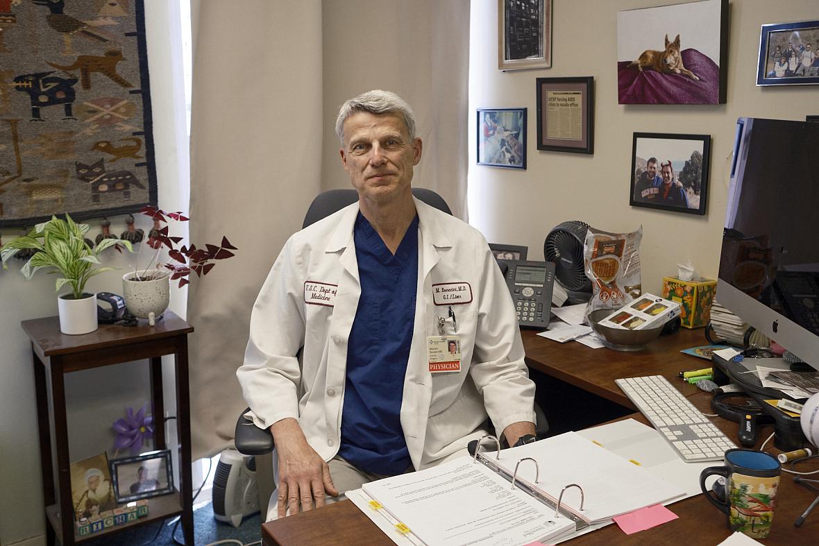 Person sitting on a desk in white lab coat with a folder open in front of him