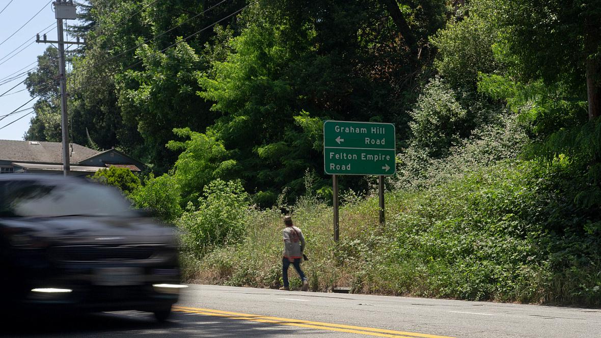 Car zooming through a road with greenery in the background and a person walking