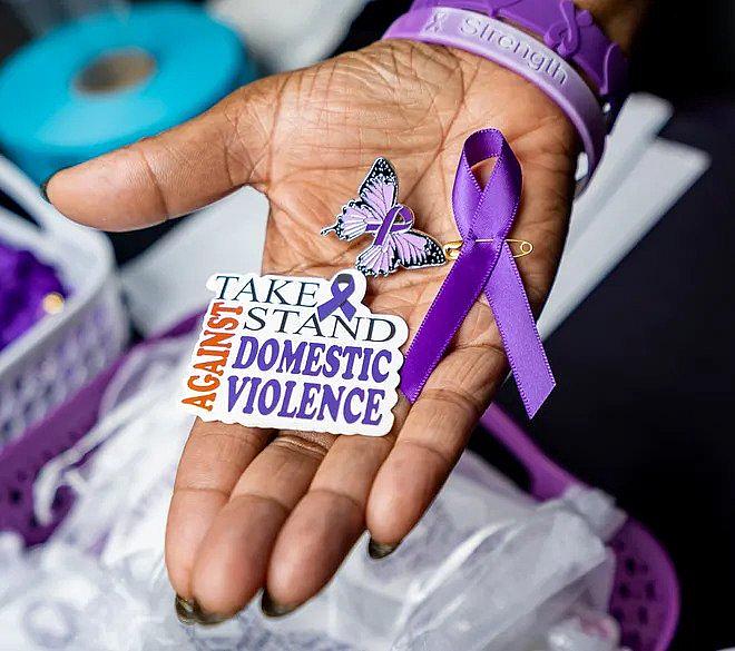 An image of a person's hand holding sticker which says "Take stand against Domestic Violence"