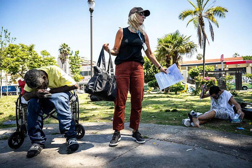 Image of a journalist in MacArthur Park in Los Angeles standing between two people struggling with homelessness and addition