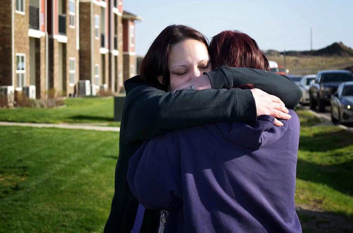 Person hugging another person against a green lawn