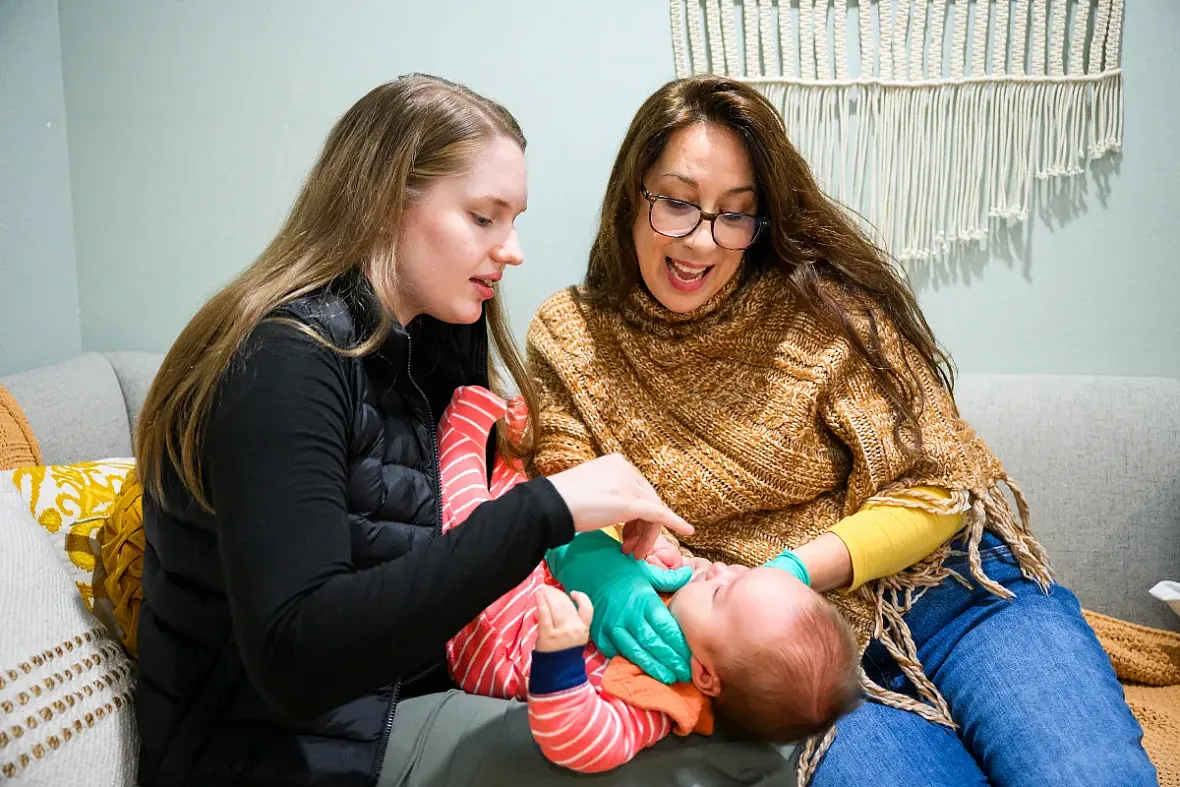 Person holding an infant and another women looking at the infant playfully