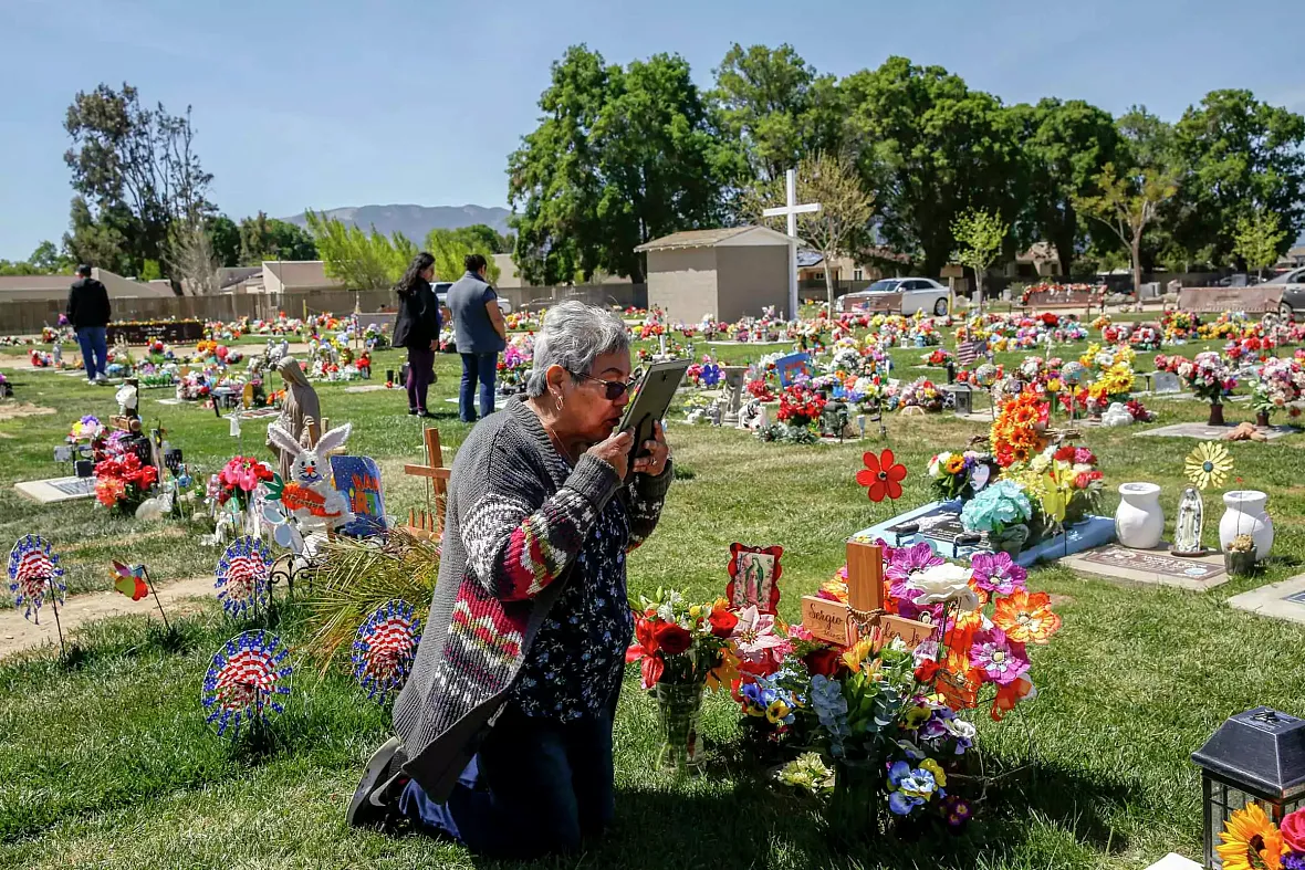 A person kissing photo of their son's in graveyard