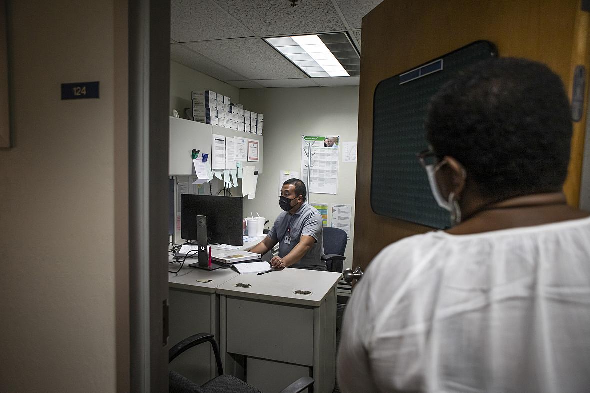 STD Investigator Hou Vang (left) works in his office as Jena Adams (right), Communicable Disease Program manager, checks in on h