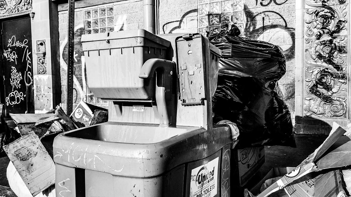 Portable sink in Skid Row missing soap dispenser surrounded by trash