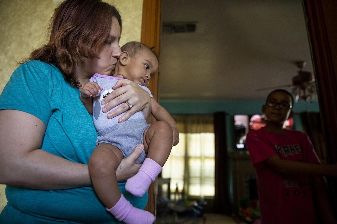 Angelica Castaneda, 30, kisses her daughter Jasmin while son, Andrew Castaneda, watches from the living room.