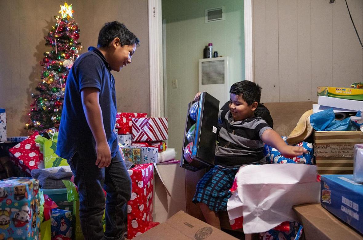 Fernando Martinez, 10, left, watches his brother, Jonathan Sanchez Jr., 6, open shiny sport balls after gifts were brought to th