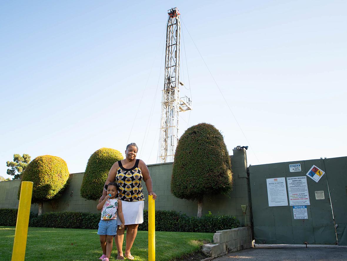 Deborah Bell-Holt and her granddaughter stand before an oil drilling site just blocks from her South Los Angeles home.