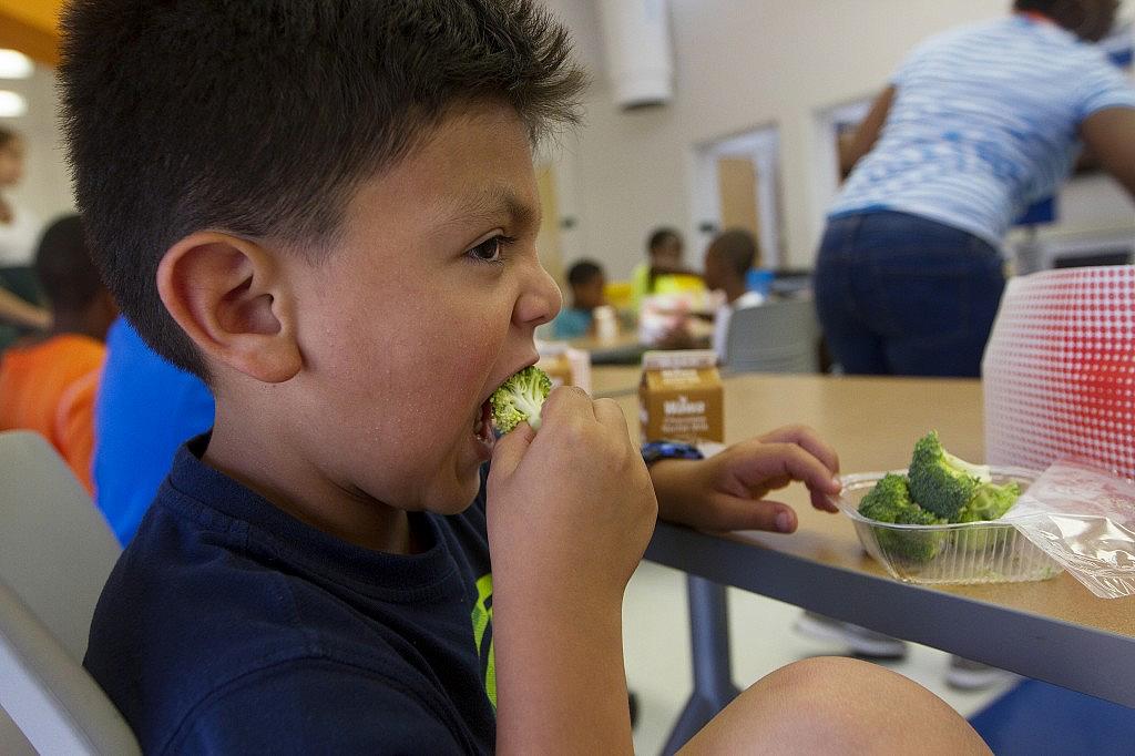 Six-year-old Jacob Portillo says he likes eating his broccoli at summer camp at Park View Recreation Center in Washington, D.C. The camp offers free lunches — funded by the USDA — to all participants and children in the community. For some, the meal fills a nutritional gap that’s crucial during the summer months when kids are out of school. Photo by Margaret Myers/NewsHour
