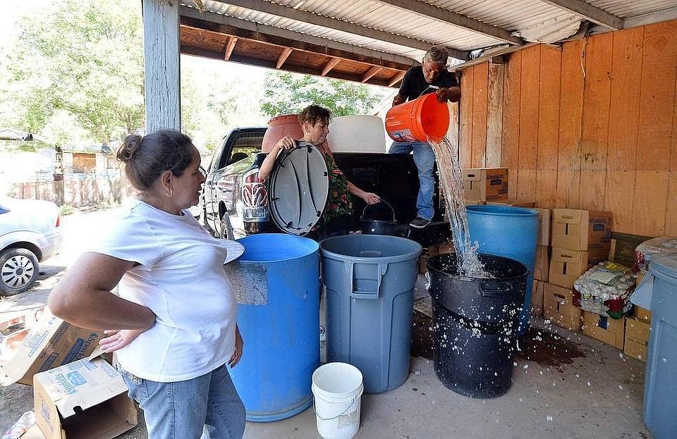 Juana Garcia, 49, watches as volunteers Donna Johnson, 72, center, and Ruben Perez, 68, deliver non-potable water to barrels on her back porch in East Porterville, California on June 4, 2015. Garcia, who suffers from lupus and arthritis, has difficulty lifting heavy objects and making the 15 minute walk with her children to a local church for showers several times a week. SILVIA FLORES sflores@fresnobee.com  