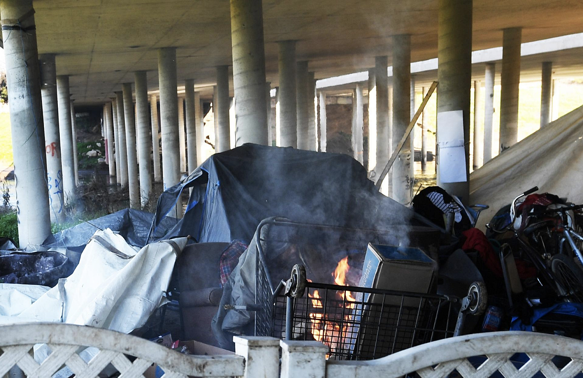 Homeless people wrap themselves in tarps as they try to keep warm near a fire at a homeless encampment beneath the El Dorado St