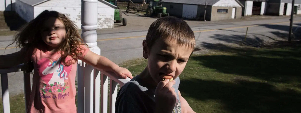 Nellie Brown, left, 6, lounges on the porch bannister as her brother Oliver, 7, fumbles with a set of toy teeth.