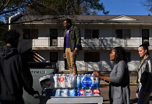 Residents place cases of water on a vehicle.