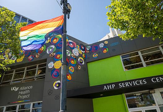 A rainbow flag flies in front of two buildings in San Francisco, including UCSF Alliance Health Project