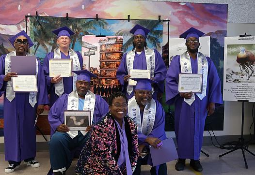 Six graduates in purple gowns hold up their diplomas