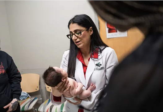 Person in a doctor's coat holding a baby