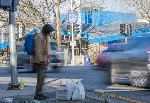 Person standing on a pavement with two plastic bags besides them