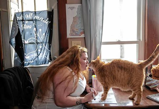 Woman leans toward orange cat on table.