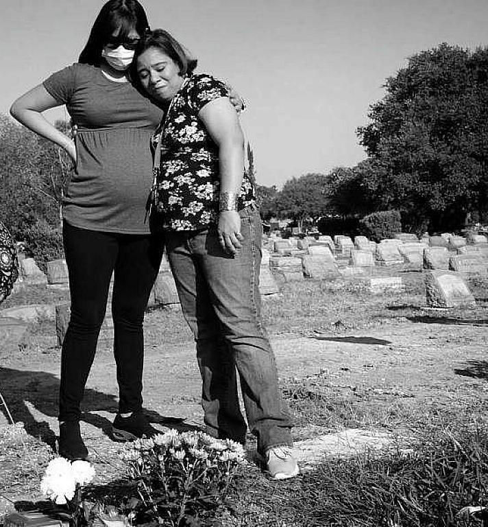 Two family members visit a grave in a cemetary.
