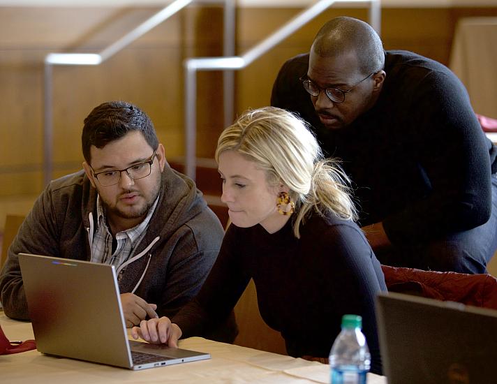 Fellows gather around a laptop and discuss.