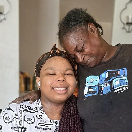 A Black woman embraces her granddaughter, who wears a prosthetic leg, in their Kern County home.