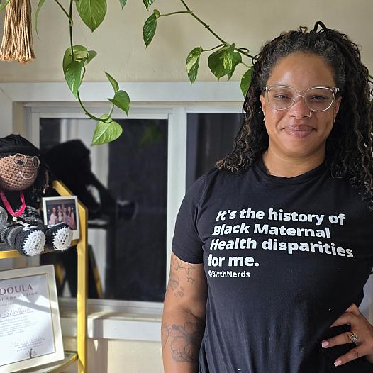 A young Black woman in glasses stands hand on hip inside a doula clinic