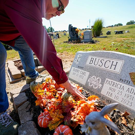 Person putting flowers on a toubstone