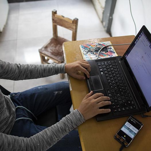 A girl on a laptop, with a cell phone on the table.