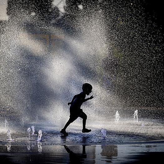 A young boy runs through a fountain.