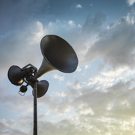 A loudspeaker silhouetted against a cloudy sky.