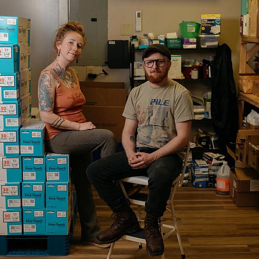 Two people sitting with a stack of needle boxes 