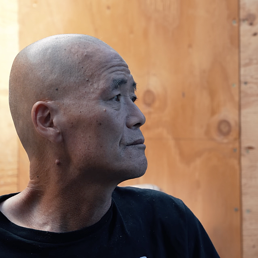An older balding Korean man sits in profile inside a community shelter in Los Angeles