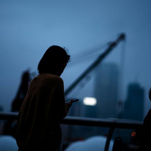 Woman looks at phone amid a dark sky background.