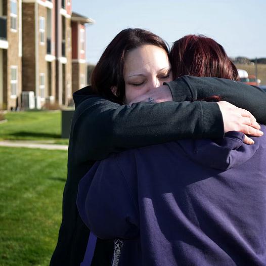Person hugging another person against a green lawn