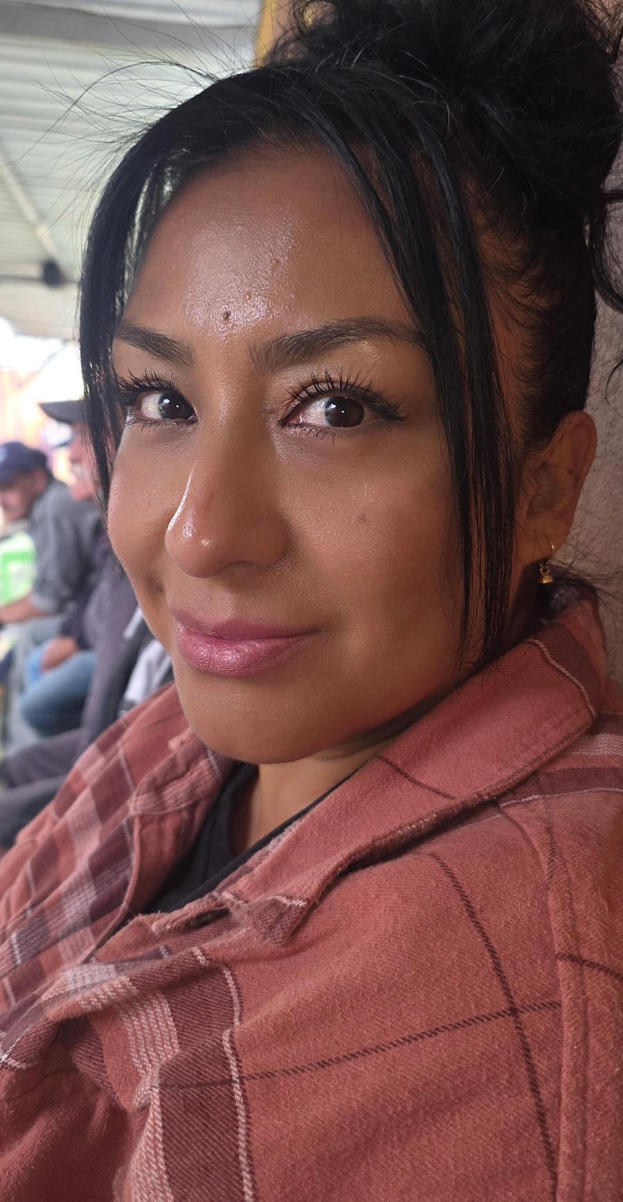 A young Latina woman smiles at the camera in pink hoodie